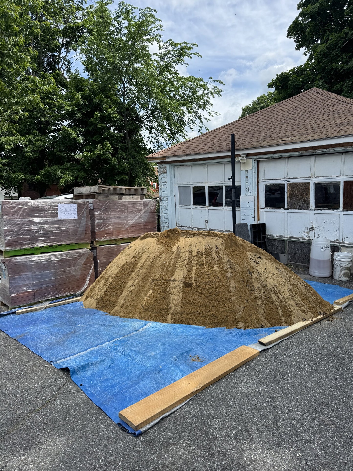 Four cubic yard pile of paver sand delivered to a residential driveway in Lowell, Massachusetts, staged next to pallets of pavers for a backyard patio install